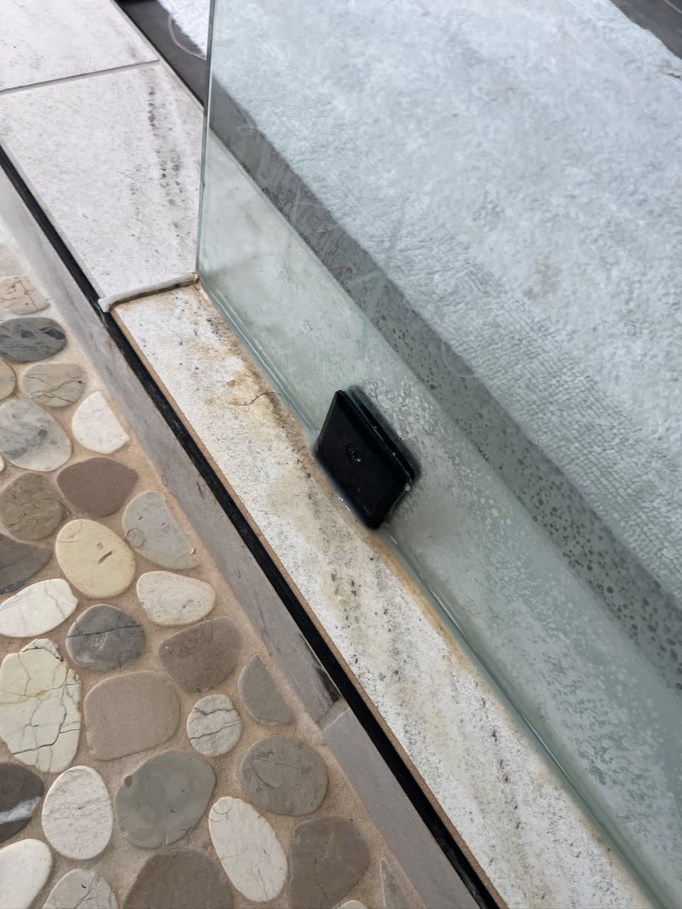 Shower glass and track with hard water buildup before cleaning